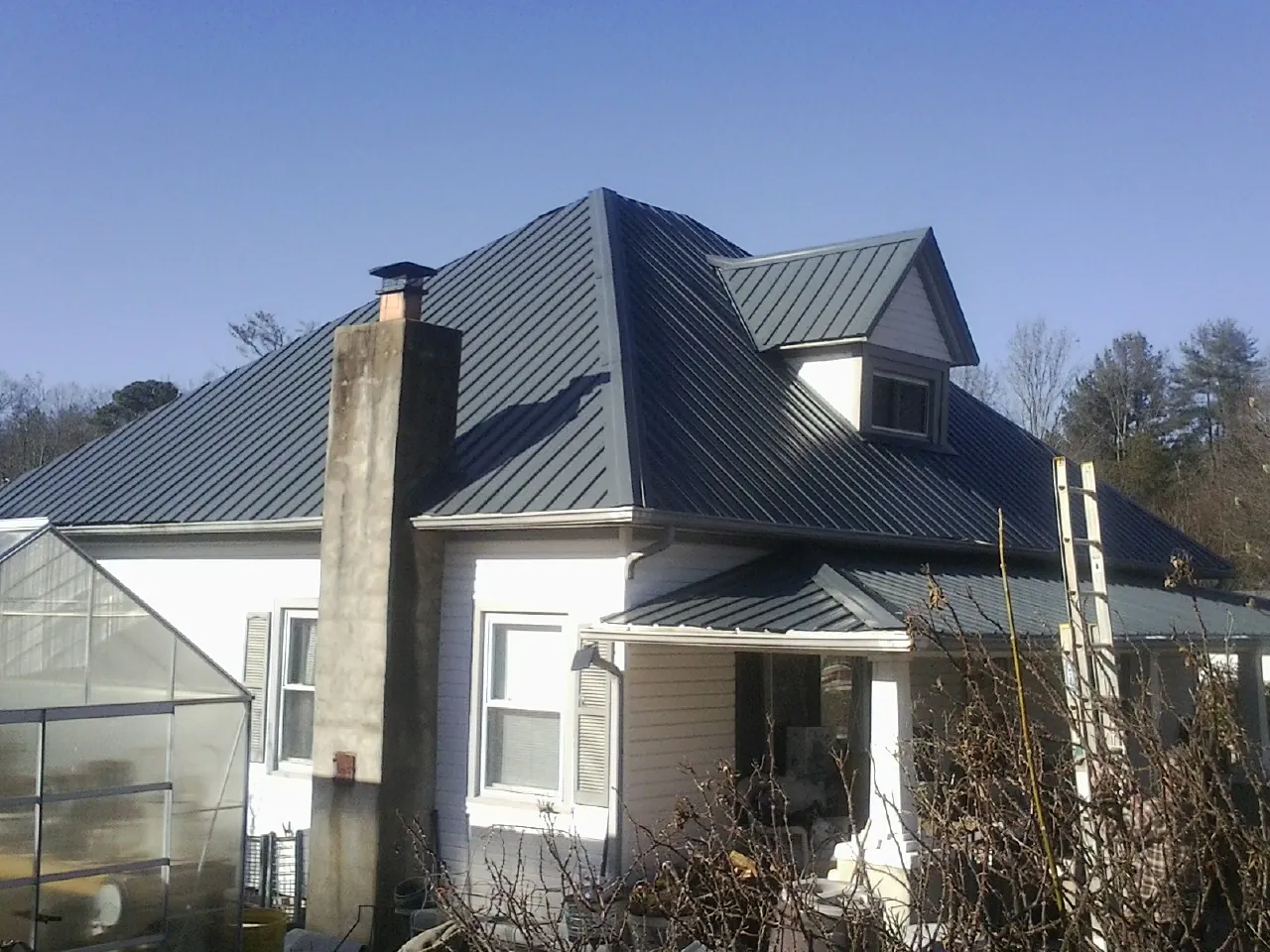 Dark blue standing seam metal roof on a white farmhouse with dormer in North Newton