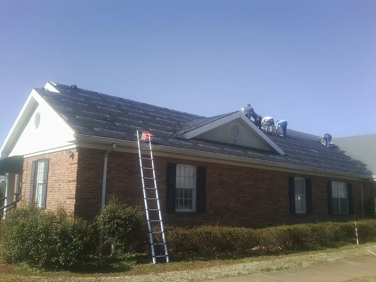 Crew tearing shingles off a brick ranch roof with a ladder set — Metal Roof Repair work by our crew in North Newton