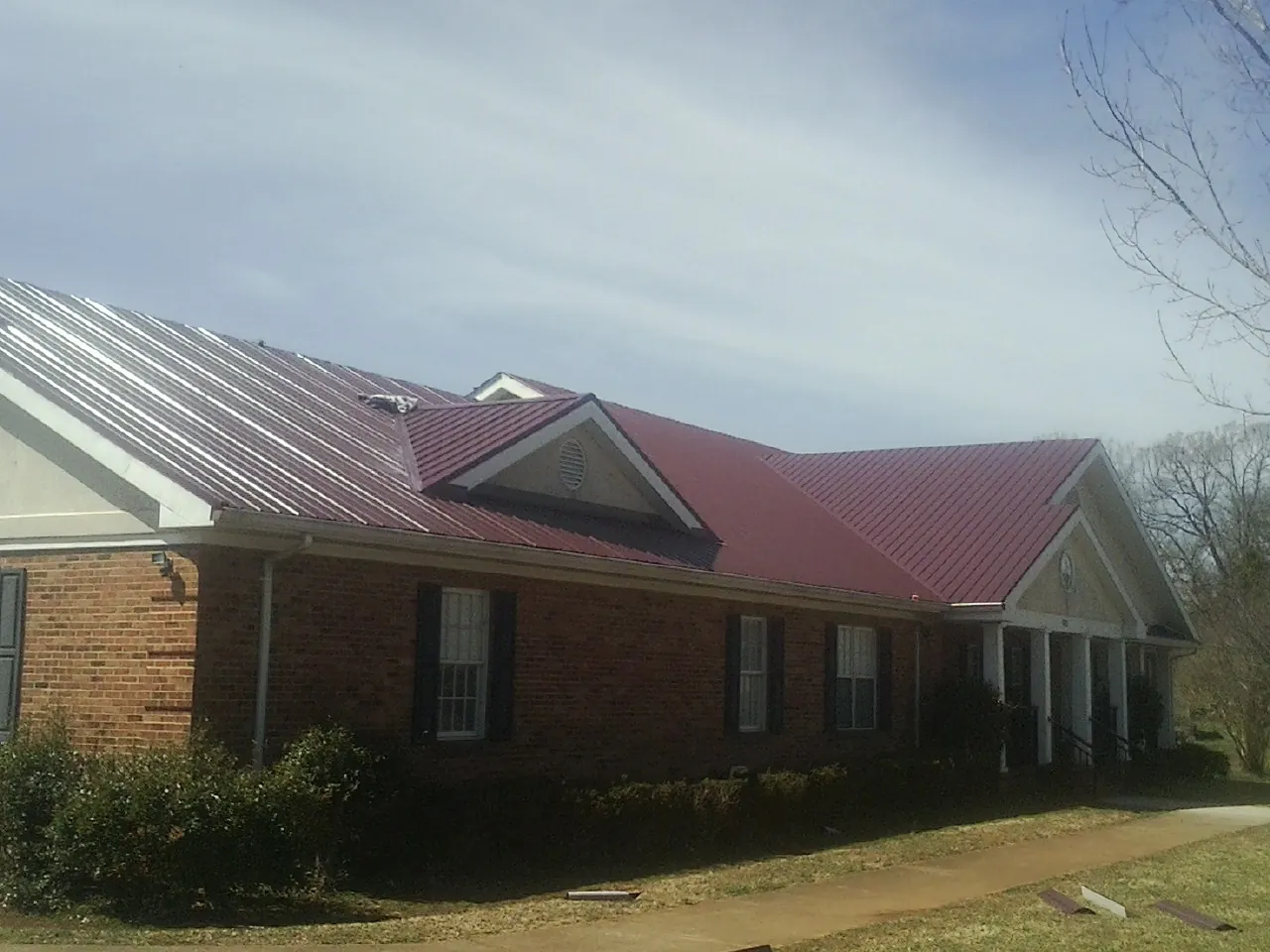 Red metal roof with gabled entries on a long brick building, from a Hail Damage Roof Repair job in North Newton
