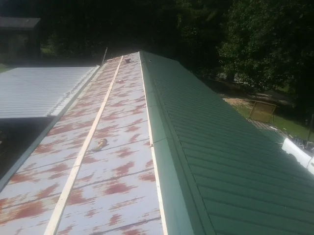 Old rusted panels beside newly installed green metal roofing — Wind Damage Roof Repair by Roofing Brothers in North Newton