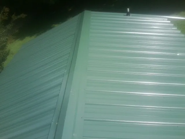 New green metal panels meeting at the ridge of a roof — Flat Roof Repair work by our crew in North Newton