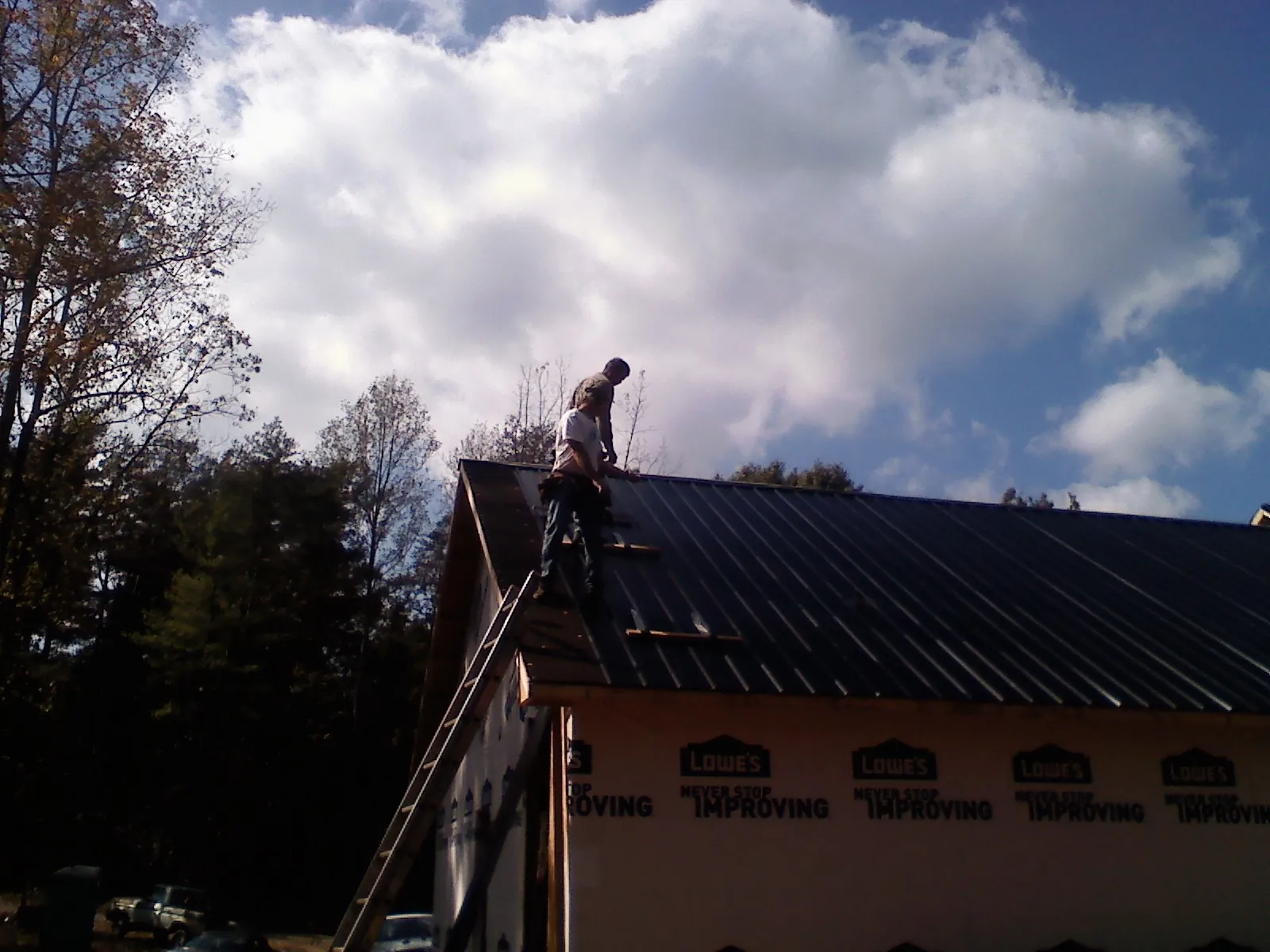 Roofer fastening dark metal panels high against a cloudy sky, from a Roof Inspection job in North Newton