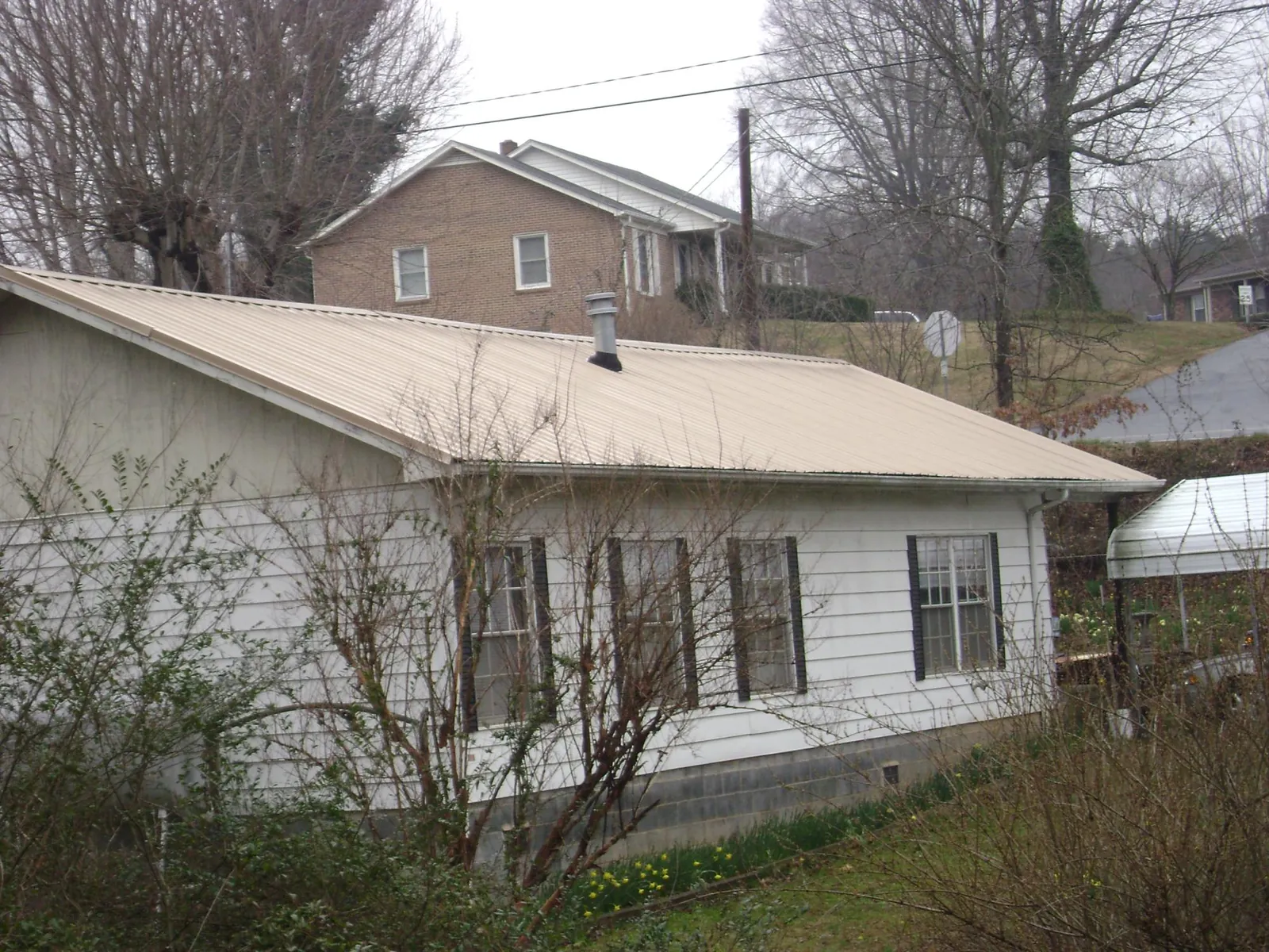 Tan metal roof on a white sided house set into a hillside — Commercial Roofing by Roofing Brothers in North Newton